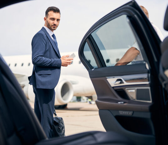Handsome brunette man in a classy suit holding his carry-on standing by a taxi cab